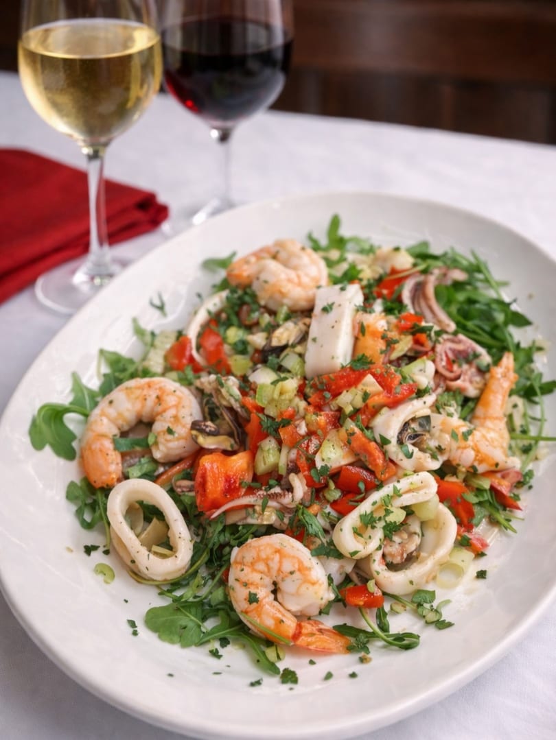 Seafood salad with shrimp, calamari, mussels, red peppers, and greens, with two glasses of wine.
