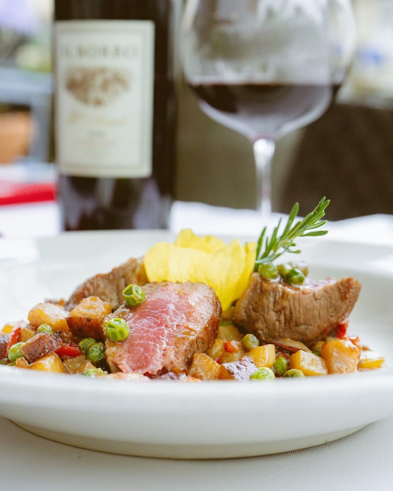 Seared steak with peas, potatoes, and rosemary, served with red wine.